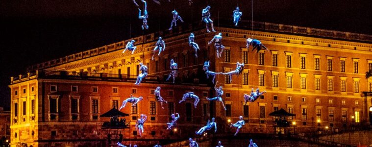 aquanauts show Caen Millennium with athletes suspended in mid air dressed in blue with building behind at night