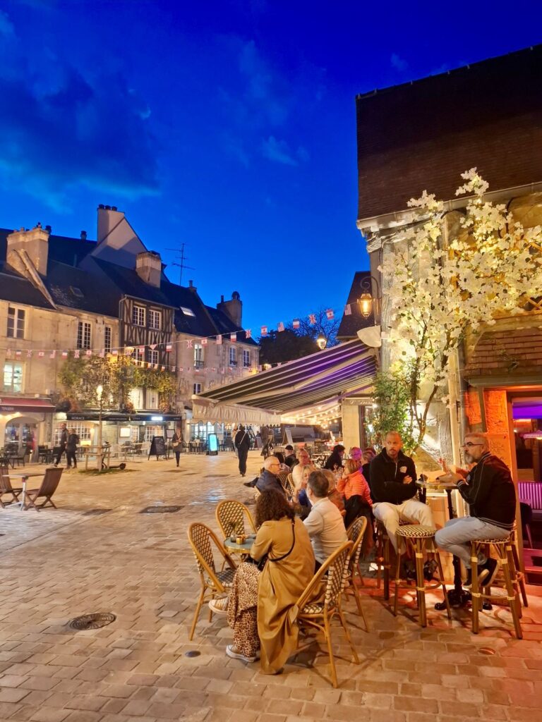 Vaugeaux restaurant in Caen at night with people sitting outside at tables and chairs, cobbled street and old houses in background