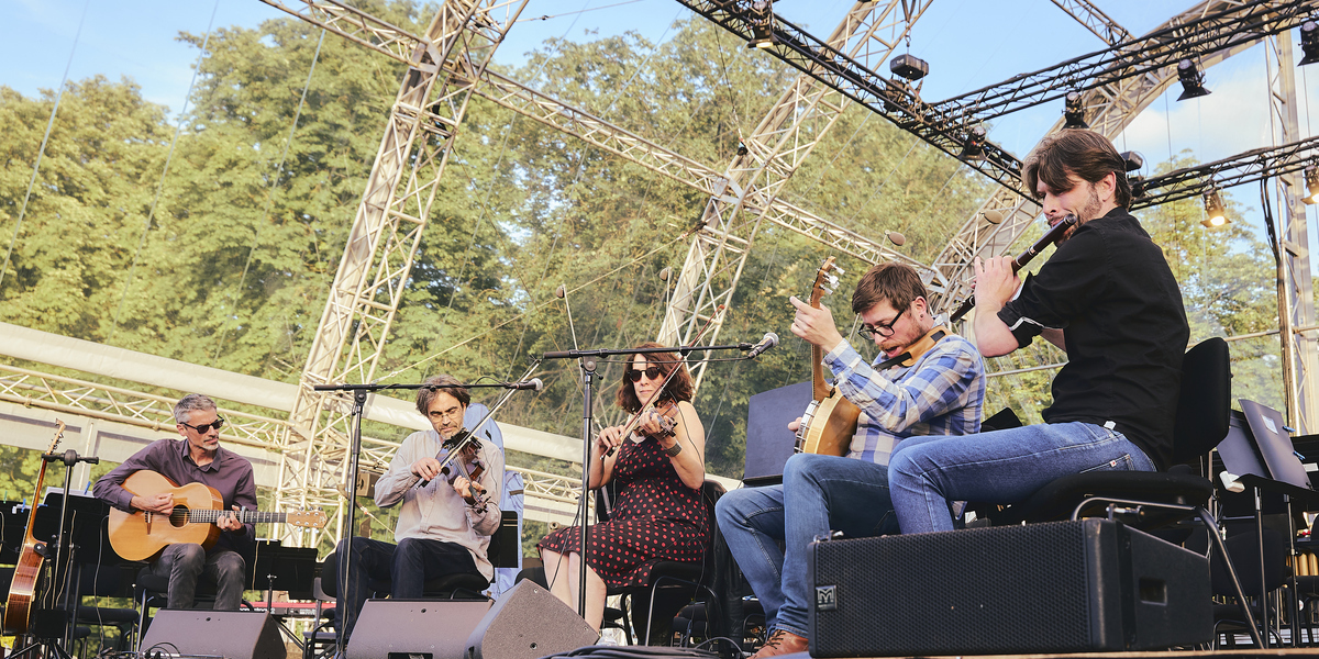 Flaneries de Reims Folk group on stage with guitars and violin in rural setting