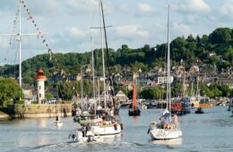 Honfleur sailors pilgrimage festival with boats sailing out of the harbour and background of town with wooded hills behind