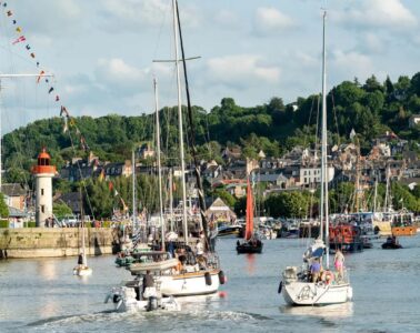 Honfleur sailors pilgrimage festival with boats sailing out of the harbour and background of town with wooded hills behind