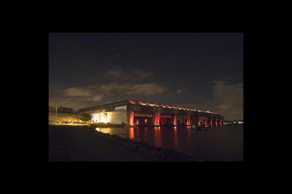 Bordeaux submarine base at night with huge concrete pens lit up and reflected in the water