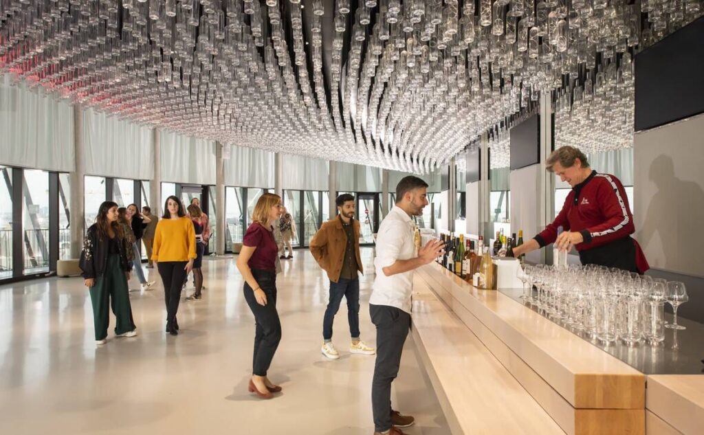 Le Belvedere wine bar on top of Le city du Vin with glasses humg from ceiling and people lined up at bar being served wine