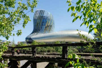Cité du vin EXTERIOR SHOWING HUGE GLASS AND STEEL BUILDINB BEHIND A FENCE WITH CURVING TOWER
