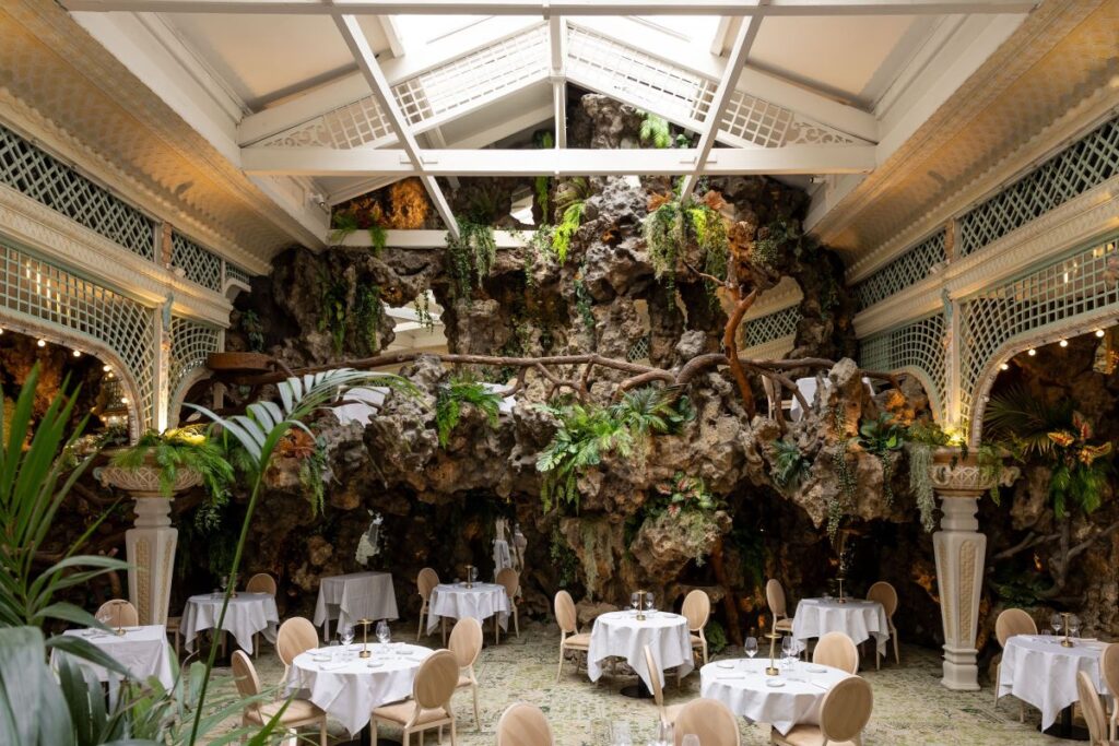 Le chapon fin interior with glass rrof, foliage and huge rocks as background to tables