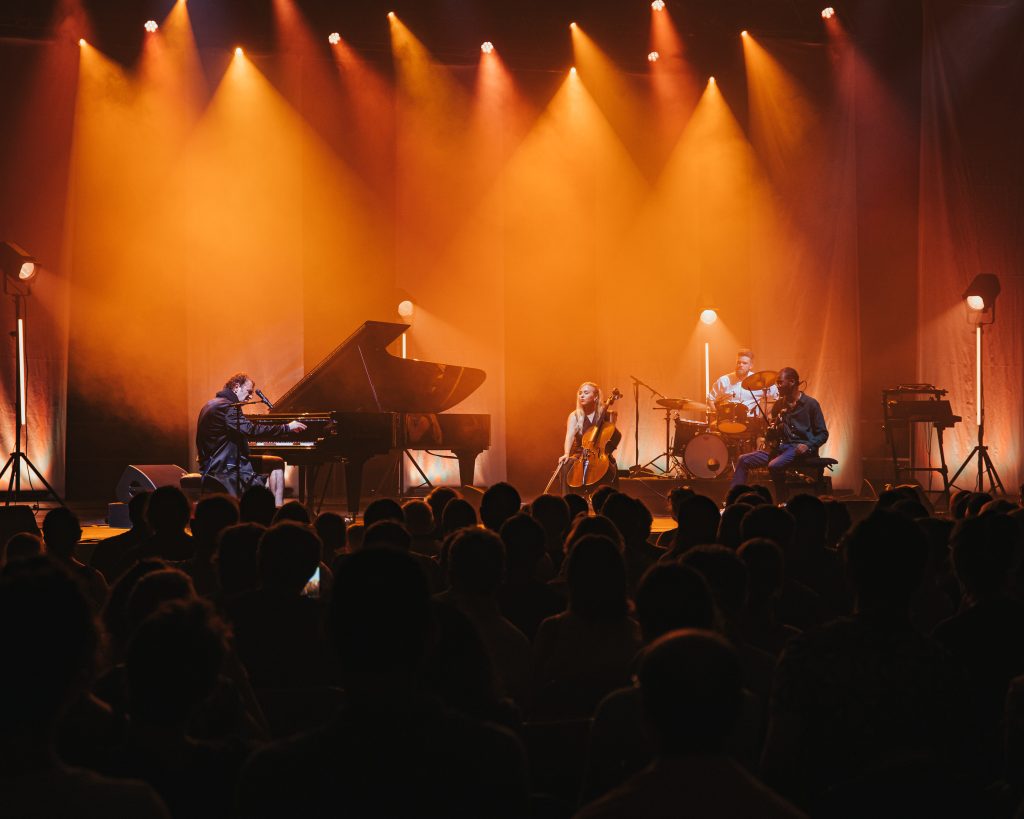 Festival of 1000 Notes with stage lit by overhead lights, grand piano with pianist and other musicians