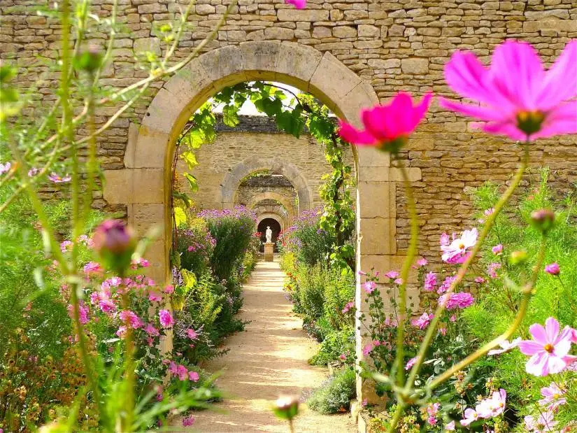 Garden view through stone arch to more stone arches beyone and flowers in beds beside path