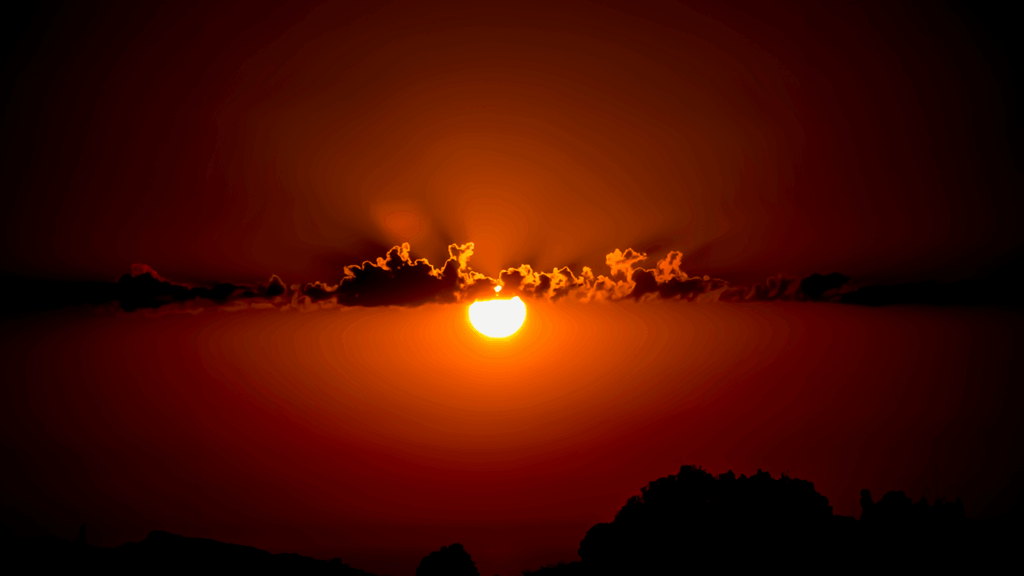 Corsica film Festival sky with sun setting below clouds, orange sky and outline of buildings and mountains at bottom