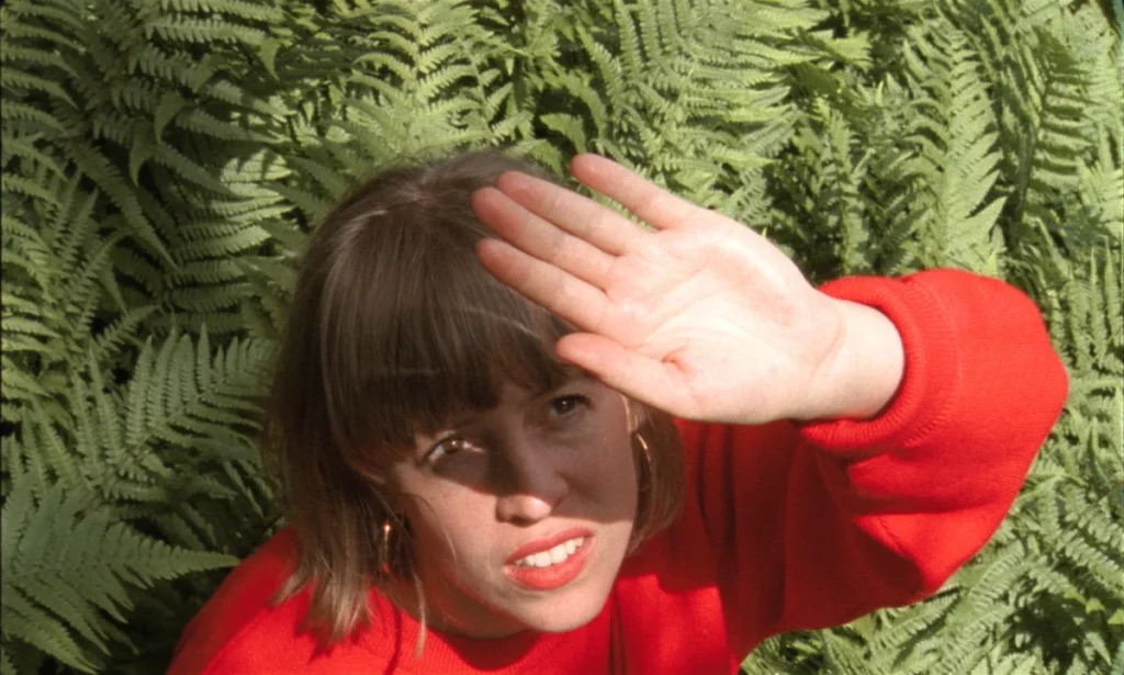 Marseille film festival with woman in red jumper looking up at sky with hand up to shield from sun and ferns in background
