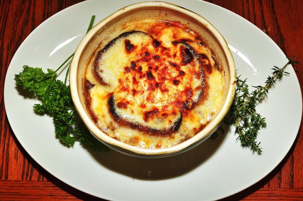 Frenchonion soup in ceramic bowl on plate with parsley beside