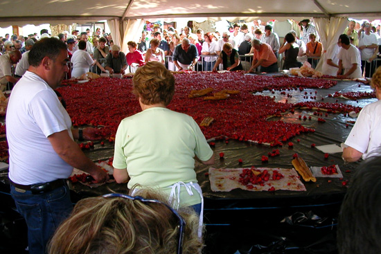Biggest strawberry tart in the world with woman standing cutting it up, tart beyond and people waiting in background