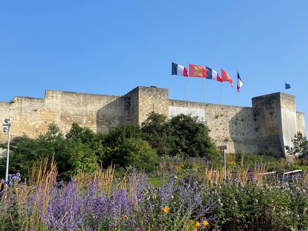Caen castle looking from flower beds up to walls with flags flying