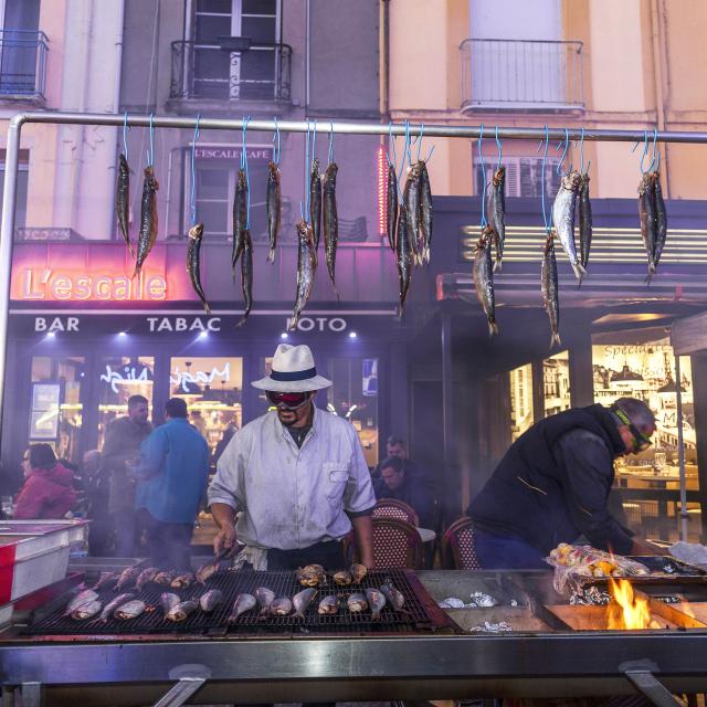 dieppe Herring Festival with man in white shirt and panama hat behind stall with herrings hanging and him cooking
