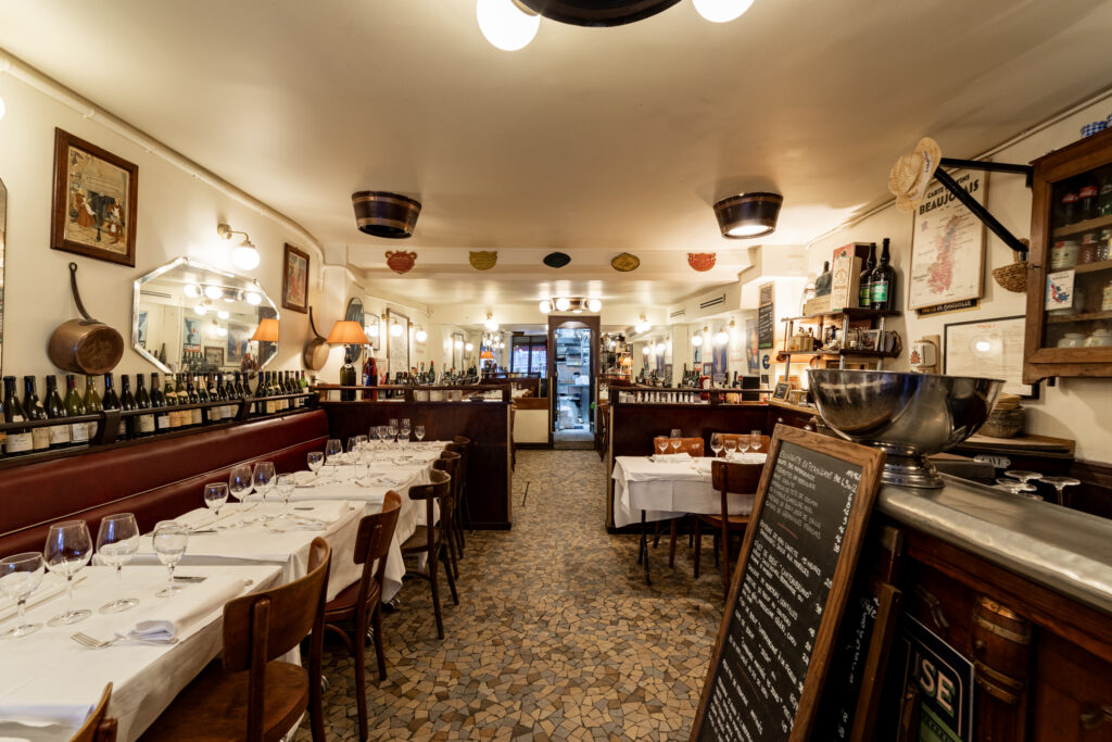 AuMoulin a Vent Paris inside with large room, blackboard with menu by bar and tables and chairs opposite