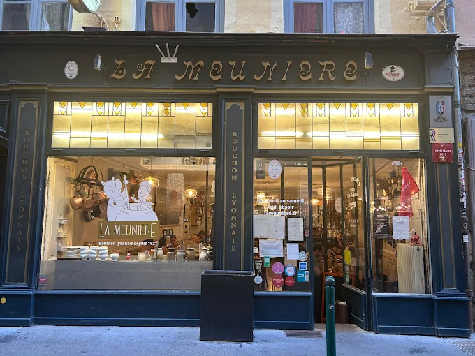 La Meuniere Lyon outside with classic front and windows showing pots and pans, tables, chairs