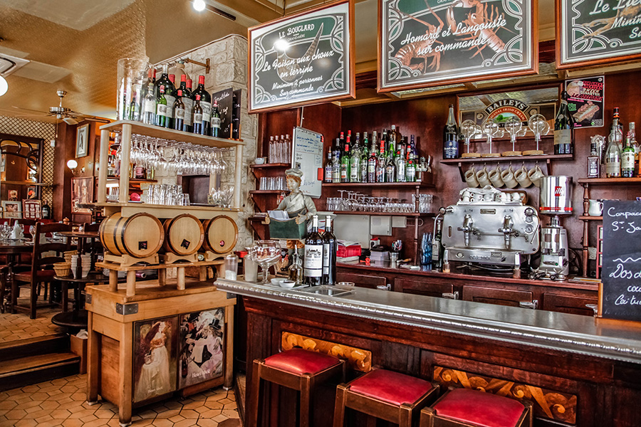 Le bouclard restaurant interior showing bar with stools in front, lots of bottles behind and busy wall