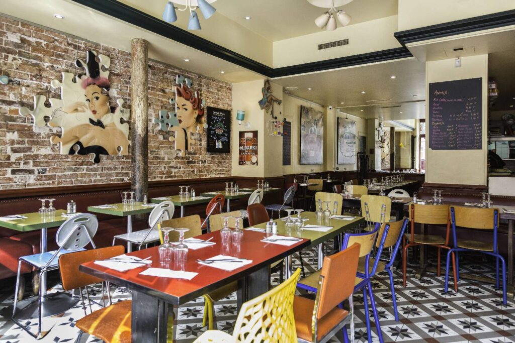 chez Gladines Saint Germain restaurant paris with funky art on walls, red topped tables, funky plastic chairs and marble floor
