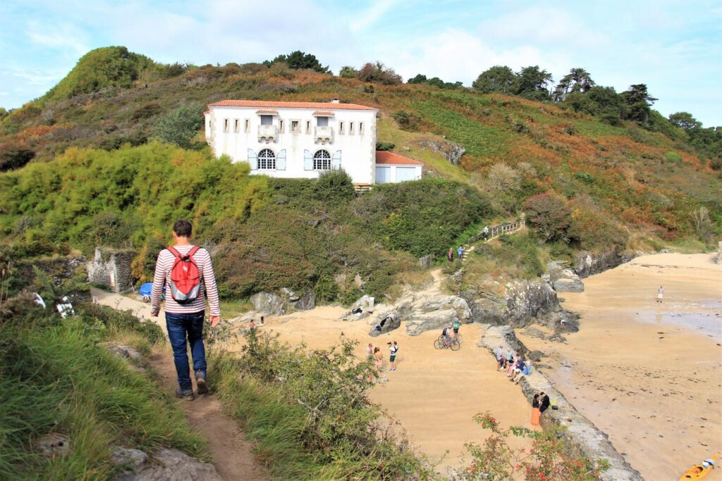 Beach at Port-Maria, Belle-Ile with white houses on slope above the beach and man on cliff in forefront walking