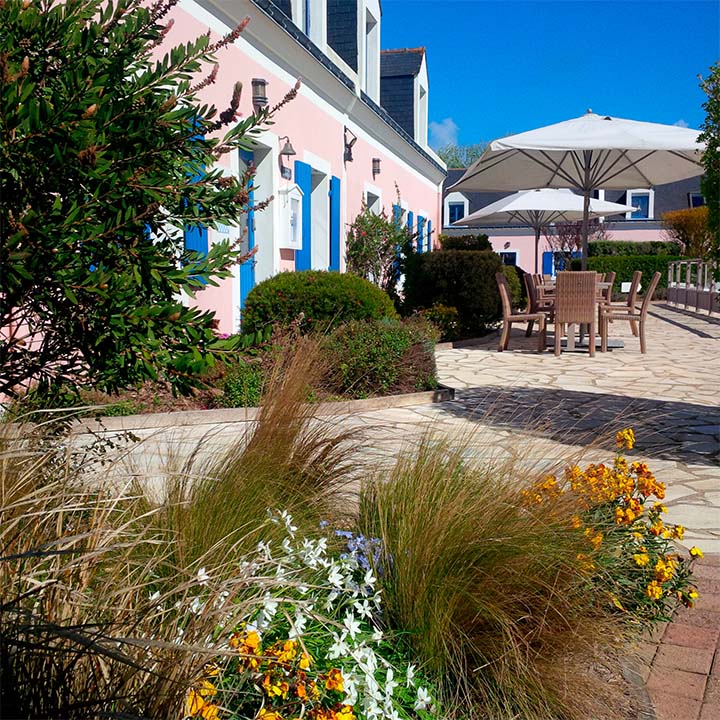 Side view of La Désirade Hotel Belle Ile with long pink walls and blue shutters and tables outside