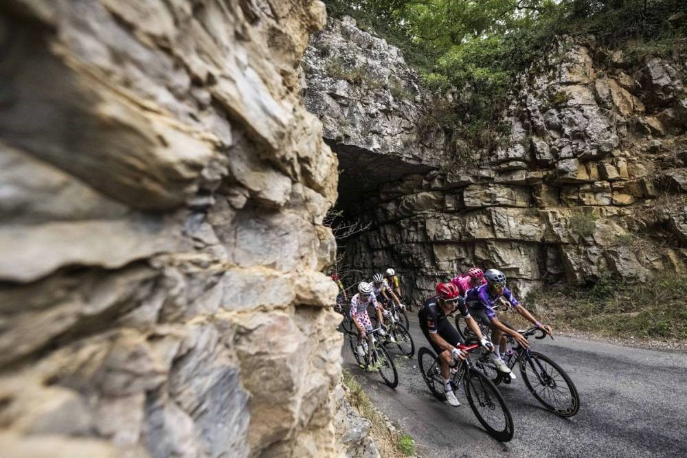 Tour de France 2025 with a few cyclists emerging from huge cave i rocky mountainside